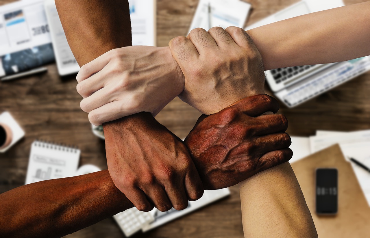 4 people from diverse background holding hands representing great team collaboration